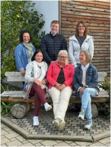 Gruppe mit sechs Personen. Drei sitzen vorne auf einer Bank, drei stehen hinter der Bank.